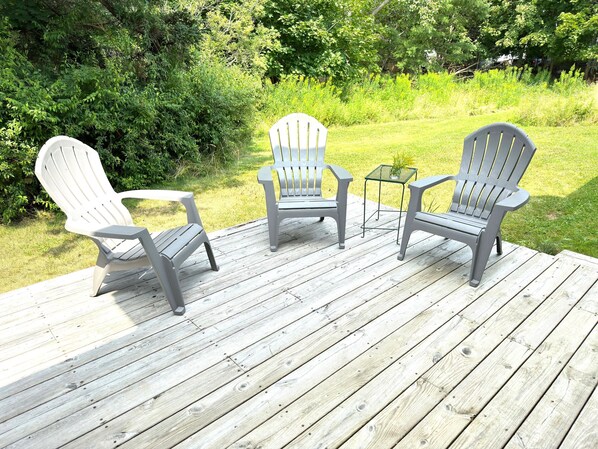 A wooden deck with three Adirondack chairs and a small table.