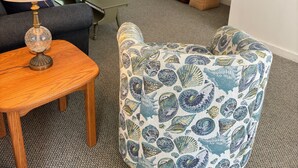 Una sala de estar con un sofá, un sillón estampado, una mesa de centro de madera, una lámpara, un televisor sobre un mueble bajo y una escalera.