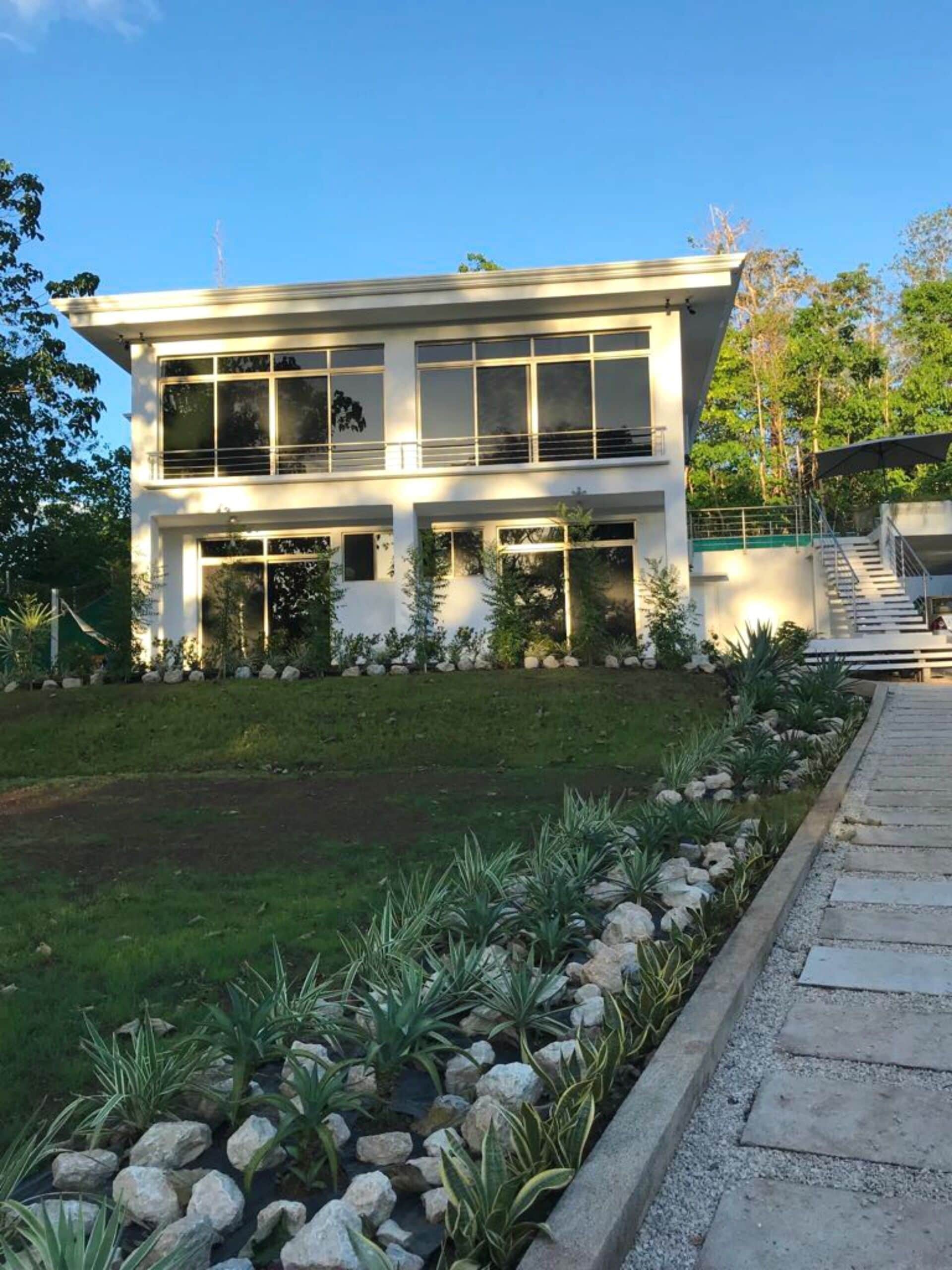 Un edificio moderno de dos pisos con amplios ventanales y un jardín cuidado con rocas y plantas.