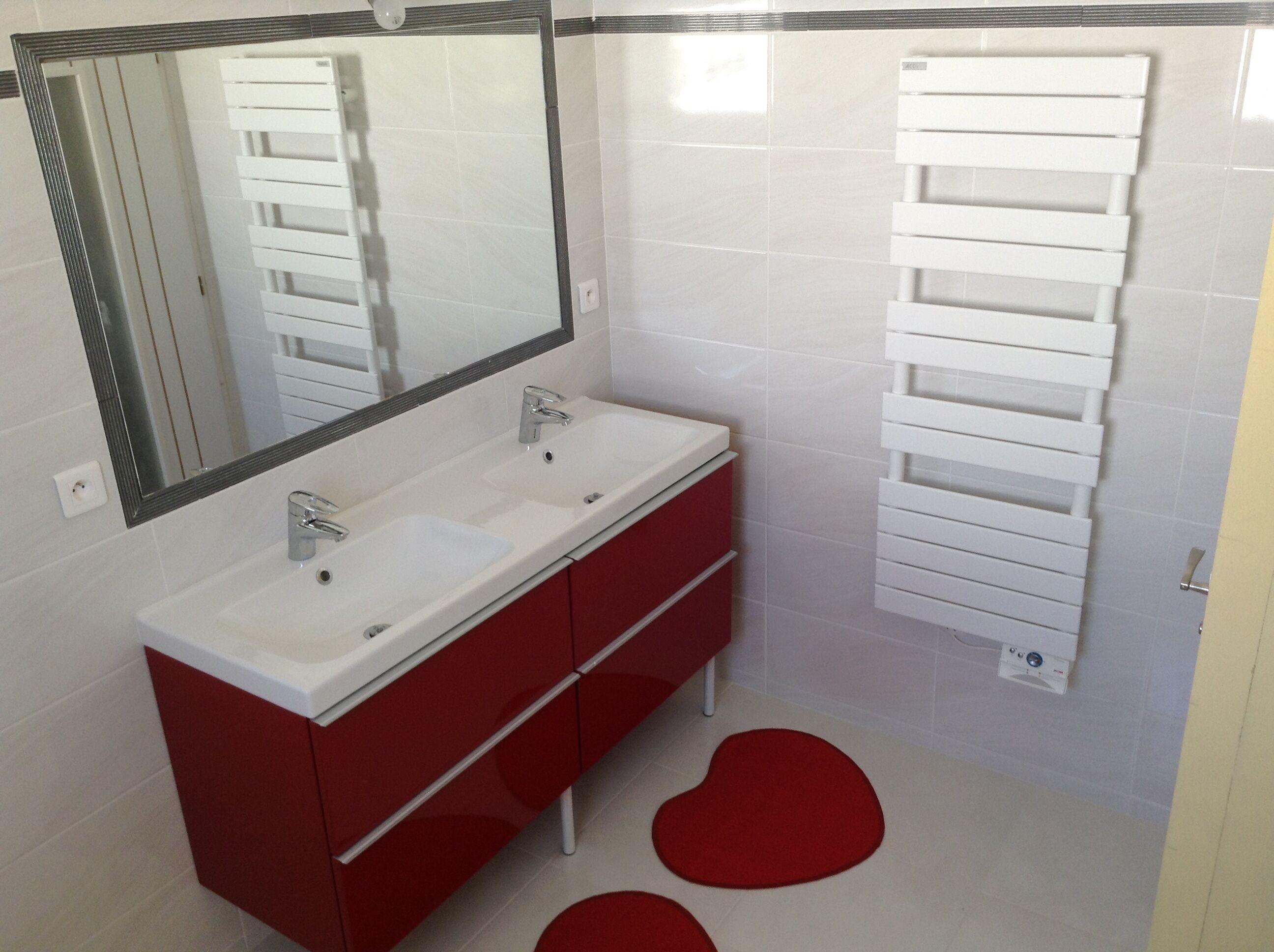 Un baño moderno con un lavamanos blanco, armarios rojos y un perchero para toallas.