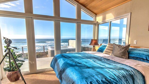 Una camera da letto con un letto grande, un treppiede con una fotocamera e vista sull'oceano attraverso ampie finestre.
