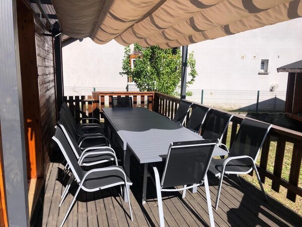 Una terraza al aire libre con una mesa larga y sillas, una valla de madera y un área cubierta.