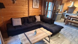 A cozy log cabin interior with a dark-colored sofa, a wooden coffee table, and a kitchen area with modern appliances. - CHALET RIVIERA "JACUZZI OFFERT" 3* wifi ANDORRA ax les thermes Orlu ski (Orlu)