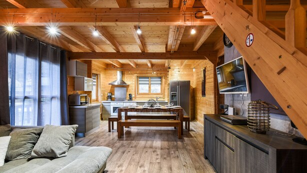 A cozy cabin-style interior with a wooden dining table, benches, a sofa, and a kitchen area. - CHALET RIVIERA "JACUZZI OFFERT" 3* wifi ANDORRA ax les thermes Orlu ski (Orlu)