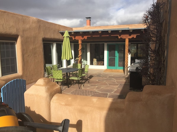 Relax in the serene patio area with a round table, green chairs, and a matching umbrella, surrounded by a pergola.