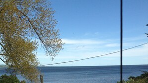 A view of a beach from a window overlooking a wooden deck and a grassy area. - Minnesota Point Beach House 1-Spectacular Lake Superior View (Duluth)