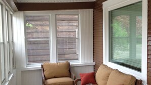 A sunroom with two wooden chairs, a small table, and a window with shutters. - Minnesota Point Beach House 1-Spectacular Lake Superior View (Duluth)