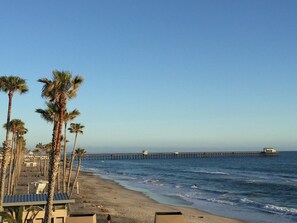 A beach with palm trees, a pier extending into the ocean, and beach facilities. - Beachfront Condo Within a tropical paradise (Oceanside)