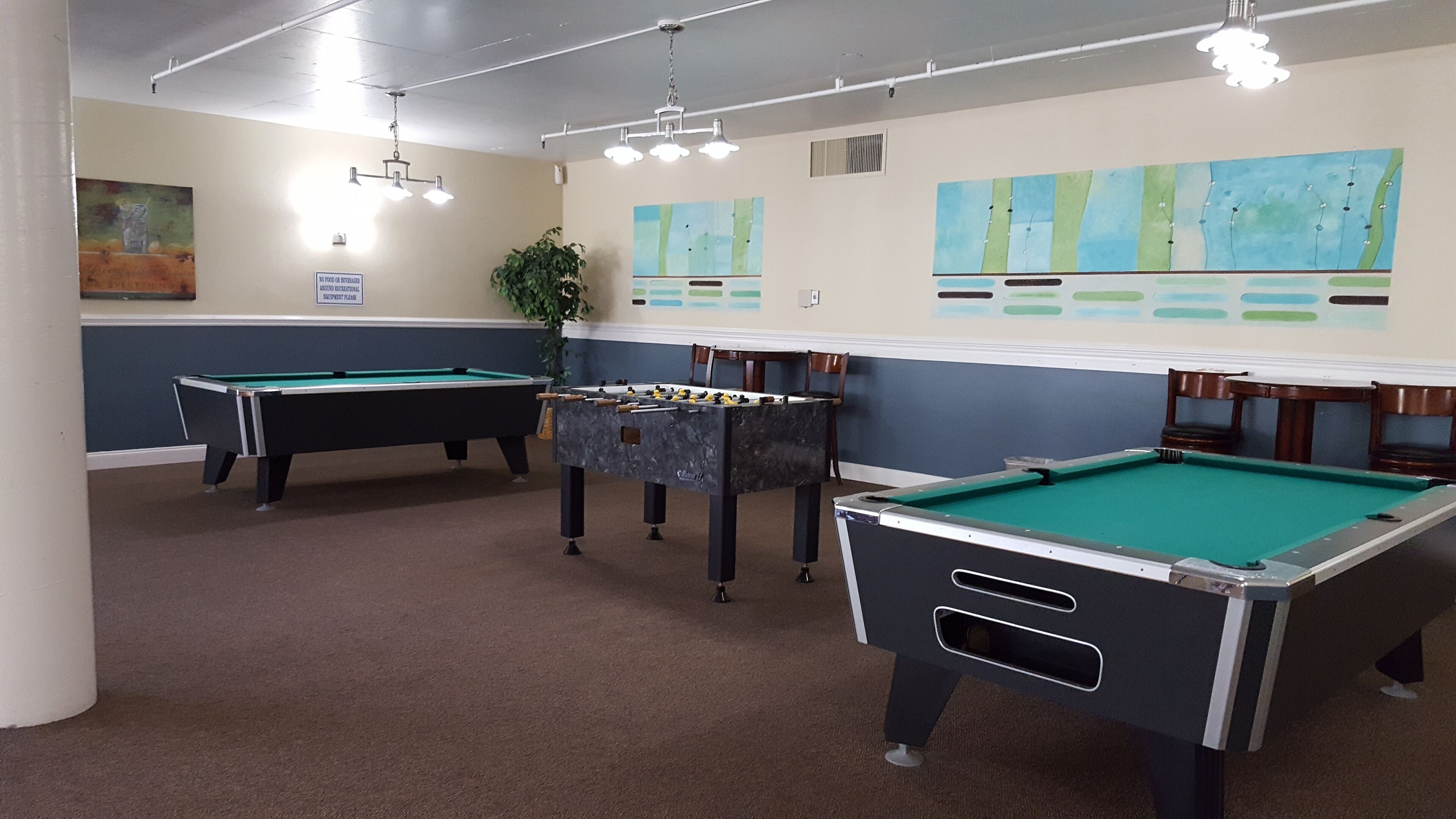 A pool room with multiple pool tables, a foosball table, and wall art.