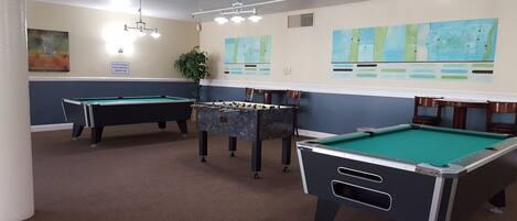 A pool room with multiple pool tables, a foosball table, and wall art.