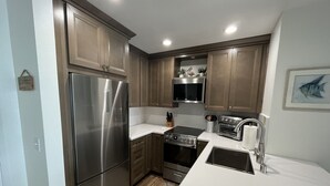 Una cocina moderna con electrodomésticos de acero inoxidable, armarios de madera y encimera blanca.