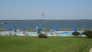 Un espace piscine agrémenté de parasols bleus, d’un drapeau et offrant une vue sur l’eau.
