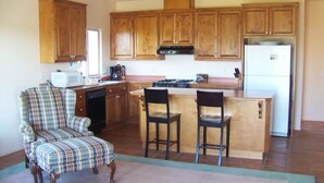 A kitchen with wooden cabinets, a dining area with a plaid sofa, and a kitchen island with two bar stools. - Lupine Ranch - Wine Country Guest House (Templeton)