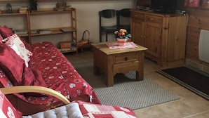 A cozy living room with a sofa, a wooden coffee table, a television, and a bookshelf. - Apartment in a quiet village (Briançon)