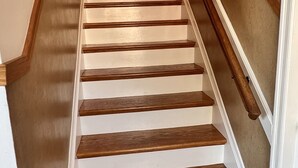 Un escalier en bois avec des marches blanches et une rampe, menant à une porte dotée d’un trou de serrure.