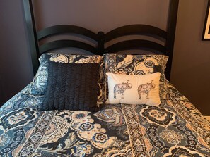 Un lit avec une couvre-lit à motifs, deux oreillers et une tête de lit sombre.