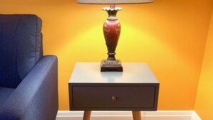Une pièce avec un fauteuil bleu, une petite table avec une lampe et un mur jaune.
