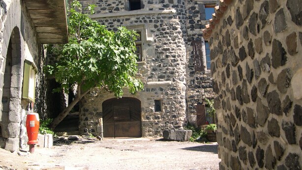 A narrow street with stone buildings, a large tree, and a wooden gate. - Separate gite without immediate neighbour on laid out field, a lot of space... (Les Granges-Gontardes)