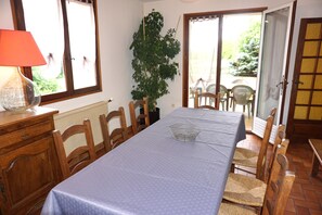 Ein Essbereich mit einem Tisch für vier Personen, Holzkstühle, einem Blumentopf und einem Fenster mit Vorhängen.
