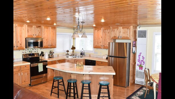 A kitchen with wooden cabinets, stainless steel appliances, a central island with stools, and a ceiling with wooden beams. - Neil's Yellowstone: Scenic Trails, Cozy Nights, Sleeps 6-9. (Island Park)