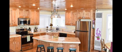 A kitchen with wooden cabinets, stainless steel appliances, a central island with stools, and a chandelier.