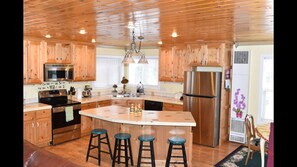 Une cuisine dotée de meubles en bois, d’appareils électroménagers en acier inoxydable, d’un îlot central avec des tabourets et d’un plafond avec des poutres en bois.