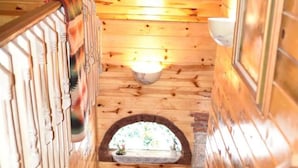 Uma escada de madeira leva a um quarto com uma pequena janela e um objeto decorativo no chão.