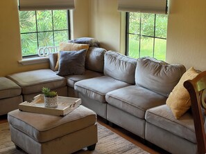 A living room with a beige sofa, a matching ottoman, and a tray with a plant.