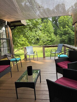 An outdoor patio with wicker furniture, a glass table, and a view of a forest.