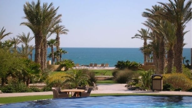 A pool area with a view of the ocean, surrounded by palm trees and lounge chairs. - Gorgeous Ocean View- completely remodeled 2/2, Great Decor, Fireplace, King Beds (Puerto Penasco)