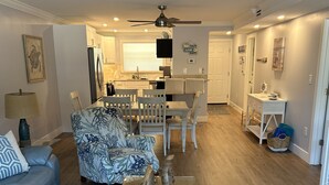 A spacious living room with a blue sofa, a patterned armchair, and a wooden coffee table. A dining area with a white table and chairs is visible in the background. - Crescent Beach Escape – 2BR Beachfront Condo on Siesta Key
Steps to the sand! (Siesta Key)