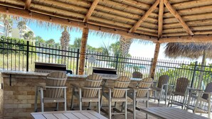 An outdoor patio with wooden tables and chairs, a barbecue grill, and a thatched roof. - Crescent Beach Escape – 2BR Beachfront Condo on Siesta Key
Steps to the sand! (Siesta Key)