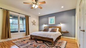 A bedroom with a wooden bed, a large window with curtains, a ceiling fan, and a star decoration on the wall.