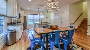 A modern kitchen with wooden countertops, a dining table with blue chairs, and a hanging light fixture.