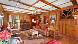 A rustic wooden interior with a high ceiling, a leather sofa, a wooden coffee table, and a cowhide rug. - 5 STAR **STRAWBERRY CORNER** CLASSIC CABIN ON CREEK, 1 MINUTE WALK TO VILLAGE! (Idyllwild)