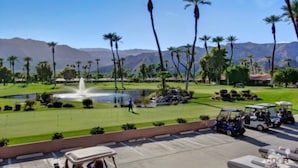 Un parcours de golf agrémenté d’une fontaine, de palmiers et avec des montagnes en toile de fond.
