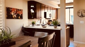 Une cuisine moderne avec des meubles de couleur bois foncé, un grand îlot central doté d’un évier et un coin repas avec une table et des chaises en bois.
