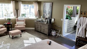 Une chambre bien éclairée, dotée d’un grand lit, d’une chaise, d’une coiffeuse et offrant une vue sur l’extérieur.