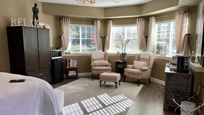 Une chambre à coucher comprenant un lit, deux fauteuils, une petite table, une armoire et une fenêtre avec des rideaux.