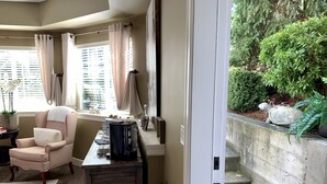 Une pièce avec un bureau en bois, une chaise, une fenêtre avec des rideaux et une vue sur un jardin avec un mur de pierre et une tortue.