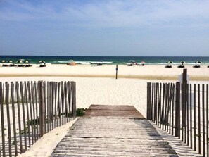 A wooden pathway leading to a beach with umbrellas and lounge chairs.