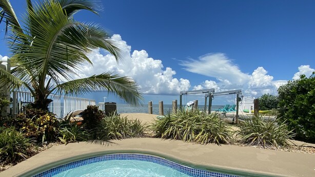 A clear blue pool with a tiled edge, surrounded by palm trees and a sandy area. - Spectacular Gulf Front Home - Pool, Dock, Incredible Gulf View (Marathon)