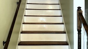 Una escalera con peldaños blancos y tablas de madera oscura, que lleva a una plataforma con barandilla blanca.