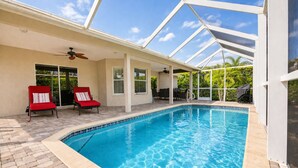 A swimming pool with a glass ceiling, two red lounge chairs, and a ceiling fan. - True Happiness In Paradise!  Close To Everything!  Heated Pool! (Marco Island)