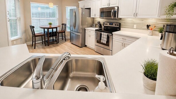 A modern kitchen with stainless steel appliances, a dining area with a table and chairs, and a view of the outside through large windows. - True Happiness In Paradise!  Close To Everything!  Heated Pool! (Marco Island)