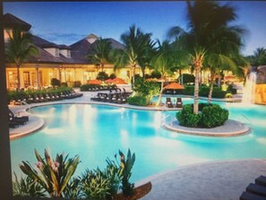 A pool area with lounge chairs and umbrellas, surrounded by palm trees and a building with a sloped roof. - Private Cabana Villa Luxury 3BR - 3BA Mustang Golf Course at Lely Resort, Naples (Naples)