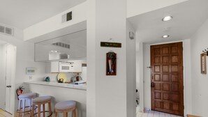 A kitchen with a white countertop, three wooden stools, a wooden door, and a sign reading "The 19th Hole". - Desert Princess Cc And Resort, On Golf Course, W/ Mountain Views (Cathedral City)