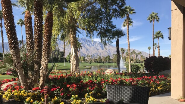A patio with a glass table, surrounded by vibrant flowers and tall palm trees, overlooking a golf course and mountains. - Desert Princess Cc And Resort, On Golf Course, W/ Mountain Views (Cathedral City)