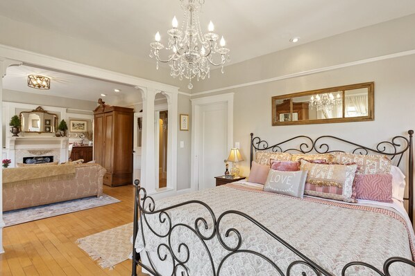 A bedroom with a large bed, a chandelier, a mirror, and a fireplace.