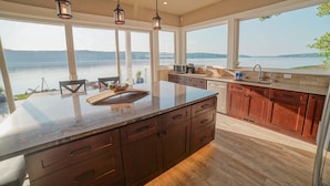 A modern kitchen with a large island, wooden cabinets, and a view of a lake.